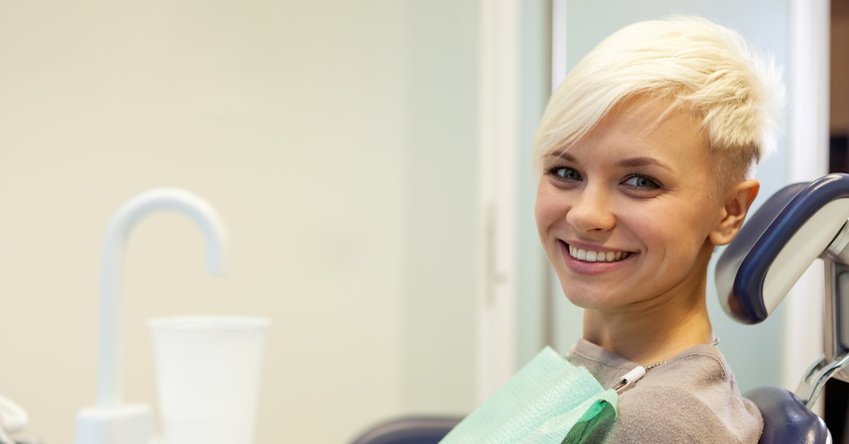 Blonde smiling woman sitting at the dentist and looking towards the camera