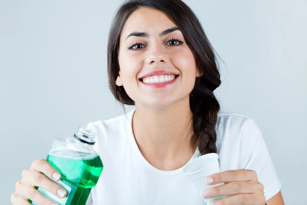 Woman holding mouthwash and cup — is mouthwash bad for you? | Blodgett Dental Care